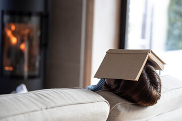 Tired woman reading a book and warming close to fireplace