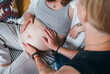 Young woman tender touching partner's female pregnant belly. Same-sex marriage couple in the home living room. Woman's health, happy pregnancy doula supporting and calm mental mood concept image.