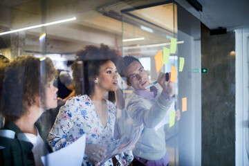 Wall Mural - Young and diverse group of people going over ideas for a project and putting notes on a window in a startup company office