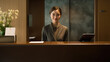 © dinastya - Young asian smiling woman pleasant looking hotel receptionist standing in her desk in reception stand.