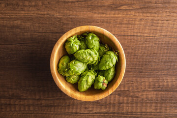 Wall Mural - Green hops crop in bowl on wooden table. Top view.