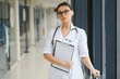 © Serhii - Portrait of young female doctor standing in hospital corridor. Caucasian woman working in nursing home.