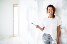 Happy Young Woman Painting An Interior Wall With A Paint Roller