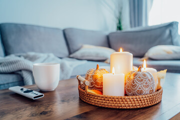 Autumn fall cozy mood composition for hygge home decor. Orange pumpkins, burning candles, cup with hot drink and remote controller on coffee table in living room. Movie night at home. Cozy relax time.