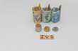 Banknotes arranged in a roll with 3 denominations of 50 zloty 100 zloty and 200 zloty next to which lie coins and zus wood inscription. The concept of early retirement, increasing the value of contrib