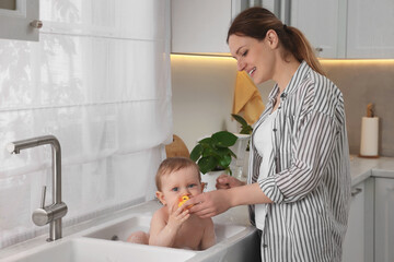 Wall Mural - Mother washing her little baby in sink at home