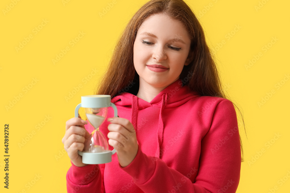Stressed young woman with hourglass on yellow background, closeup. Deadline concept