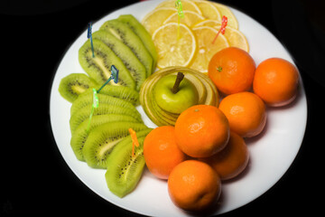 Wall Mural - Fruit white plate with tangerines, kiwi, sliced apple and lemon slices on background isolated black