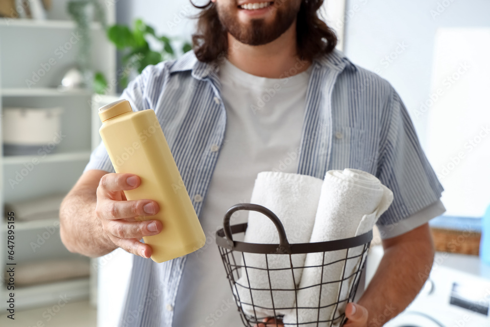 Young man with laundry basket and detergent at home
