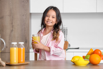 Canvas Print - Little Asian girl with fresh juice and plate of different citruses at table in kitchen