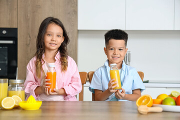 Canvas Print - Little Asian children with bottles of fresh citrus juice sitting at table in kitchen