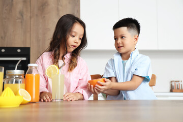 Canvas Print - Little Asian children with glass of fresh citrus juice and grapefruit slice sitting at table in kitchen