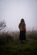 A woman in a yellow jacket looking out to the fog in a field on cold winter morning
