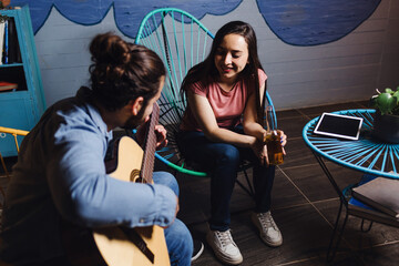 Wall Mural - young latin couple playing guitar in a romantic date, Girlfriend and boyfriend singing in home at night in Mexico Latin America, hispanic people