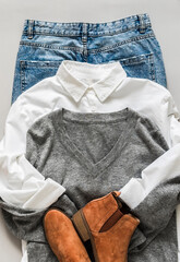 Wall Mural - Women's clothing - mom's jeans, white cotton shirt, gray pullover, suede boots on a gray background, top view