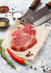 Wall Mural - Red raw beef rib eye steak fillet with steel hatchets on light background with salt and pepper.