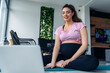 © DusanJelicic - Young pregnant woman in blue and pink sportswear communicates via video call on laptop sitting on yoga mat in living room