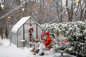 Man and woman have romantic dinner, while sitting together by the table at beautifully decorated snowy backyard. Young family celebrating winter holidays