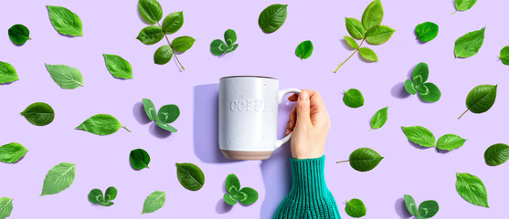 Wall Mural - Person holding a mug with green leaves - flat lay