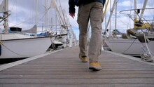 Slow Motion Low-angle Shot Of A Man Walking Along A Marina Dock Toward A Yacht