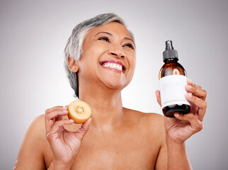 Poster - Kiwi, skin care and a woman with product for dermatology, cosmetics and wellness glow. Happy mature female person with fruit and bottle for facial treatment, nutrition and beauty on a grey background