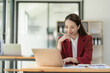 © ArLawKa - Asian businesswoman working with papers and laptop sitting at table in office, analyzing business accounting calculations and financial planning concepts.