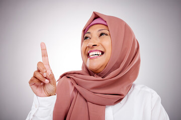 Poster - Pointing up, happy and face of Muslim woman in studio with makeup, cosmetics and beauty. Fashion, style and and Islamic person with hand gesture for news, promotion and show on gray background