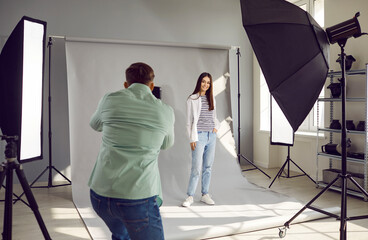 Male photographer shooting model in modern lighting studio. Rare view of photographer taking pictures with digital camera, model posing for photograph during photo shoot