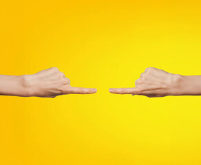 Wall Mural - Two hands pointing at each other on a yellow background with copy space