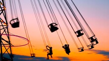 Unrecognizable Silhouettes Of People Ride On The Chained Carousel Against The Warm Evenning Sky At Sunset With At Amusement Park. Entertainment, Summer, Fun And Holiday Concept