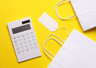 white calculator with shopping bags and price tag on yellow background. sale concept