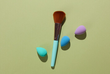 Wall Mural - Makeup brushes and make up sponges on green background. Beauty concept