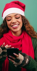 Wall Mural - Beautiful young woman in Santa hat texts and uses phone laughing, Xmas studio