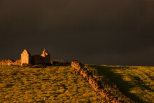 Dark Storm Clouds Over Building Ruins And A Stone Fence Along A Field At Sunset; Yorkshire Dales England