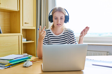 Teenage girl high school student in headphones having video conference on laptop