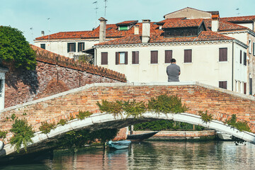 Wall Mural - Unidentified man on a stone bridge in Venice, Italy. Traditional italian local scene.