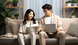 © visoot - Asian couple sitting on a couch working on laptops.