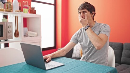 Wall Mural - Young hispanic man using laptop leaning on table to sleep at laundry facility