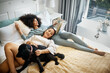 Dog, bed and happy lesbian couple in home, morning and relax together reading book. Pet, bedroom and gay women with animal, bonding and play in healthy relationship, love connection and interracial