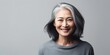 beautiful asian mid-age woman with grey hair smiling on grey background