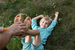 man's hands tickle a child's bare feet lying on the grass. Fun family time together, happy childhood. son's day. The joy of communication, playing around with dad. Top view, selective focus