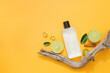 A glass perfume bottle displayed on orange background with halves of lime, green leaves and dry twig. Mockup bottle for design packaging. Copy space