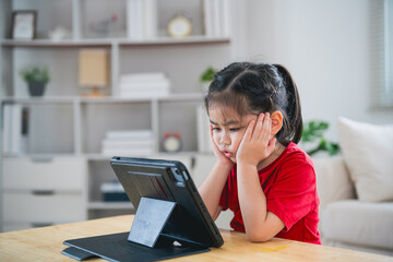 Wall Mural - Asian child girl serious to looking using and touch tablet display screen. Baby smiling funny time to use tablet. Too much screen time. Cute girl watching videos while tv, Internet addiction concept.