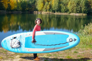 Wall Mural - Active woman with SUP board near beautiful lake, nature on background, stand up paddling water adventure outdoors, sport and healthy lifestyle concept
