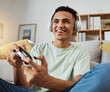 © Mumtaaz D/peopleimages.com - Home, game controller and man with headphones, relax and connection on a couch, sound and internet. Happy person, gamer and guy on a sofa, playing online and headset with audio, smile and esports
