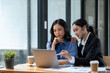 © crizzystudio - Two Asian businesswomen discuss investment project work and planning strategy Brainstorm together Find information online on iPad Laptop and tablet for making reports and summarizing business results