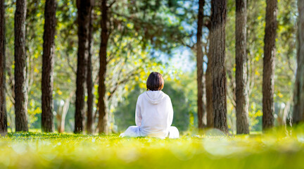 Woman relaxingly practicing meditation in the pine forest to attain happiness from inner peace wisdom with beam of sun light for healthy mind and soul concept for healthy mind and soul