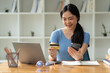 © crizzystudio - Young Asian woman using credit card and mobile phone transaction for online shopping with laptop browsing. online payment concept