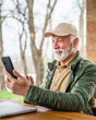 © Miljan Živković - One senior man sit in front of tiny house in day use smart phone