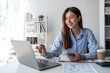 © crizzystudio - Happy young asian female accountant Positive concept using smartphone at her desk to relax with mobile application and use to chat business contact online marketing Excellent profit.